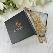 Carica l'immagine nel visualizzatore di Gallery, Gold necklace in a 'Mercy Made!' box on a light wooden surface with flowers in the background
