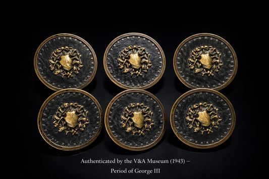 Six decorative metal buttons with a central emblem, authenticated by V&A Museum, on a black background.