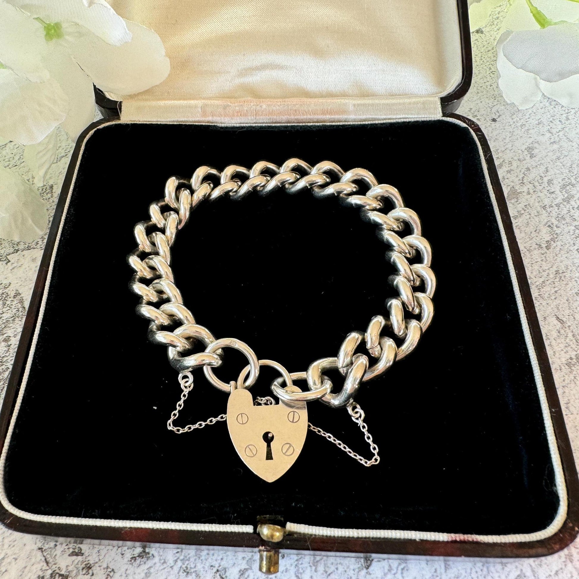 May include: A silver charm bracelet featuring a heart-shaped padlock charm. The bracelet is made of thick, chunky links and is presented in a black velvet box.